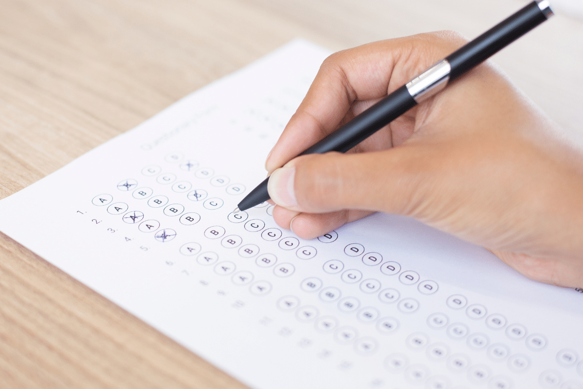 Mão segurando caneta preta preenchendo gabarito de prova de múltipla escolha.