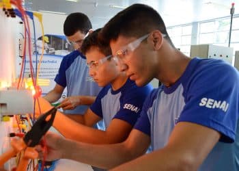Três jovens estudantes do SENAI usando óculos de proteção praticando instalação elétrica em painel