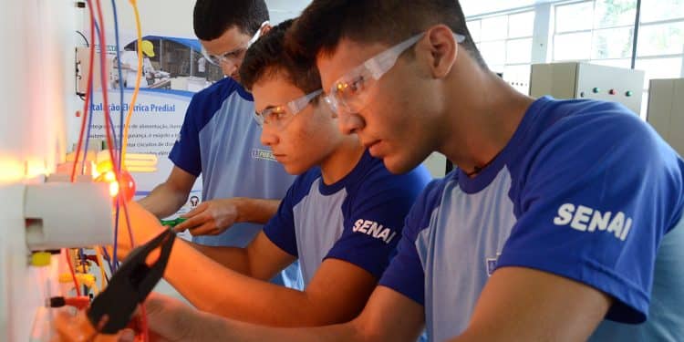 Três jovens estudantes do SENAI usando óculos de proteção praticando instalação elétrica em painel
