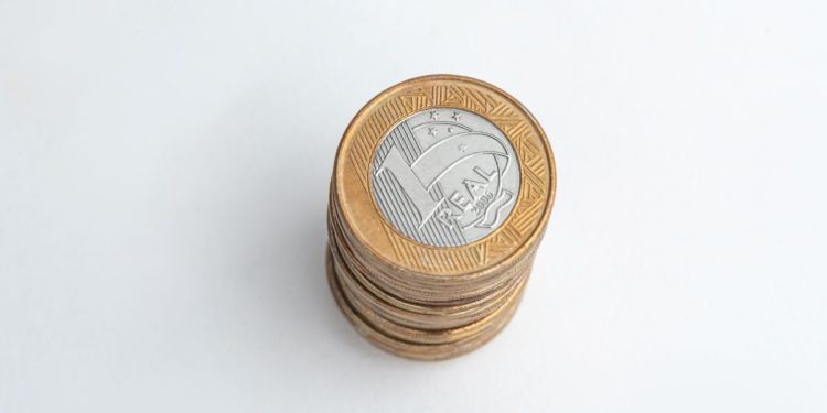 Pilha de moedas brasileiras de 1 Real sobre uma superfície branca, representando um valor potencial oculto no troco do dia a dia.