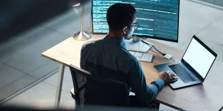 Programador focado trabalhando em código à noite com dois monitores, representando a busca por novas habilidades digitais e o avanço profissional em tecnologia.