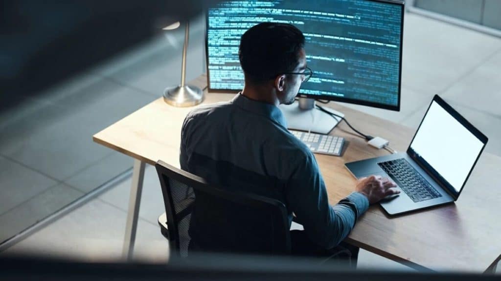 Profissional especialista em privacidade de dados trabalhando em seu computador com código. Ilustra a carreira com salário de R$ 17 mil e rotina de baixo estresse.