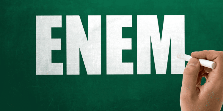 Mão segurando giz escreve a palavra ENEM em quadro verde.