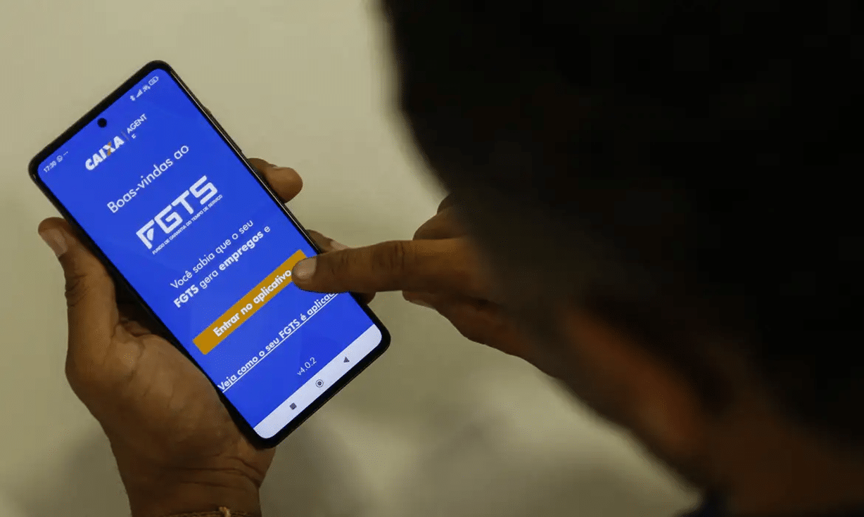 Pessoa segurando celular e acessando o aplicativo FGTS da Caixa Econômica.