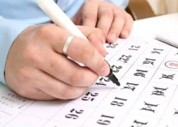 Detalhe de uma pessoa usando uma caneta para marcar datas em um calendário de papel, ilustrando a organização de folgas para o feriado de 20 de novembro (Consciência Negra) em 2025.