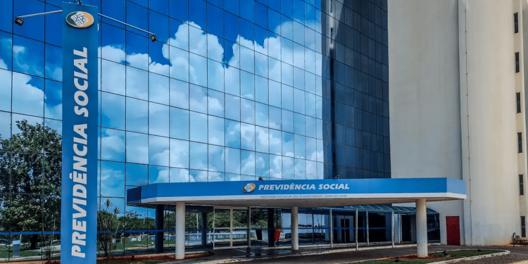 Fachada espelhada do prédio da Previdência Social com refletores azuis e céu com nuvens refletido.