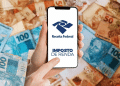 Pessoa segura celular com o logo da Receita Federal e as palavras “Imposto de Renda”, sobre fundo com notas de real.