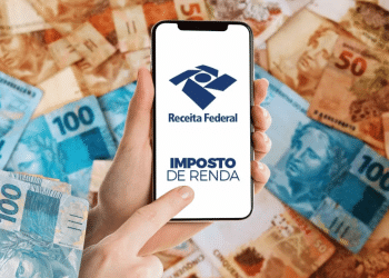 Pessoa segura celular com o logo da Receita Federal e as palavras “Imposto de Renda”, sobre fundo com notas de real.