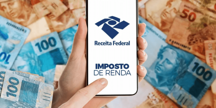 Pessoa segura celular com o logo da Receita Federal e as palavras “Imposto de Renda”, sobre fundo com notas de real.