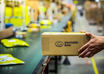 Pacote do Mercado Livre sendo manuseado em esteira de centro de distribuição, ilustrando o fluxo logístico rápido e eficiente para motoristas parceiros.