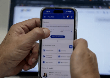 Mão segurando celular com app Meu INSS aberto mostrando consulta de benefício e serviços.