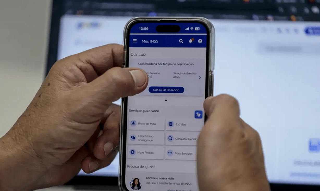 Mãos segurando celular com tela do aplicativo Meu INSS aberta, exibindo opções de serviços e consulta de benefício.