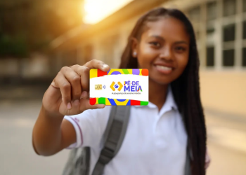 Estudante segurando um cartão do programa Pé-de-Meia com fundo escolar desfocado.