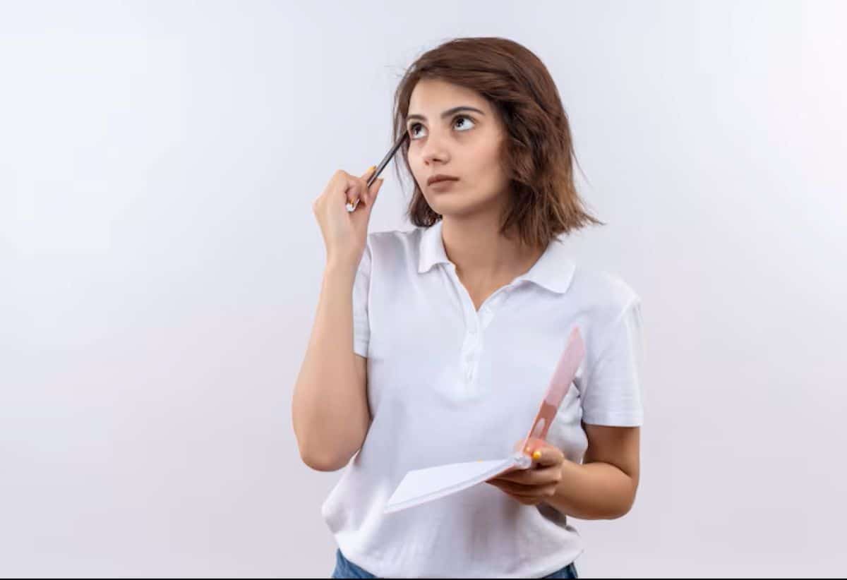 Mulher jovem e pensativa com caderno e caneta, ilustrando a busca por exemplos práticos do plural de "mau-caráter".