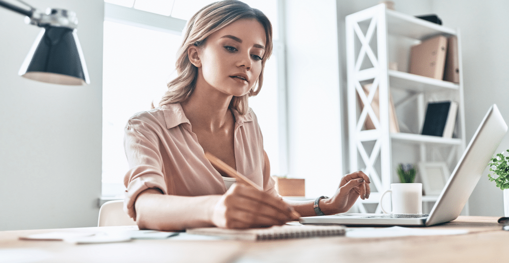 Mulher empreendedora concentrada escrevendo em seu notebook, refletindo o esforço do início de um negócio.