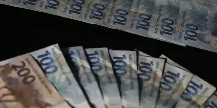 Sequência de notas de cem e duzentos reais enfileiradas representando pagamento extra governamental de até R$ 1.518