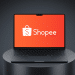 Laptop aberto com tela exibindo o logo branco Shopee sobre fundo laranja