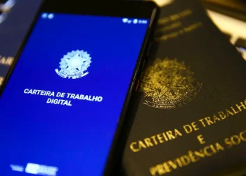 Smartphone exibindo a Carteira de Trabalho Digital ao lado de uma Carteira de Trabalho e Previdência Social física.
