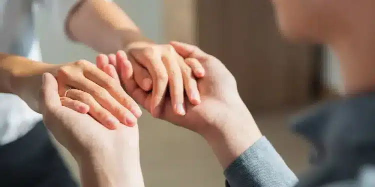 Duas pessoas segurando as mãos demonstrando apoio, confiança e empatia em ambiente interno.