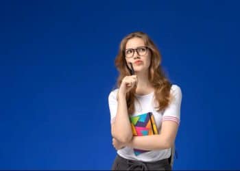 Jovem estudante pensativa, com óculos e caderno, representando a dúvida sobre a forma correta do plural de "mau-caráter".