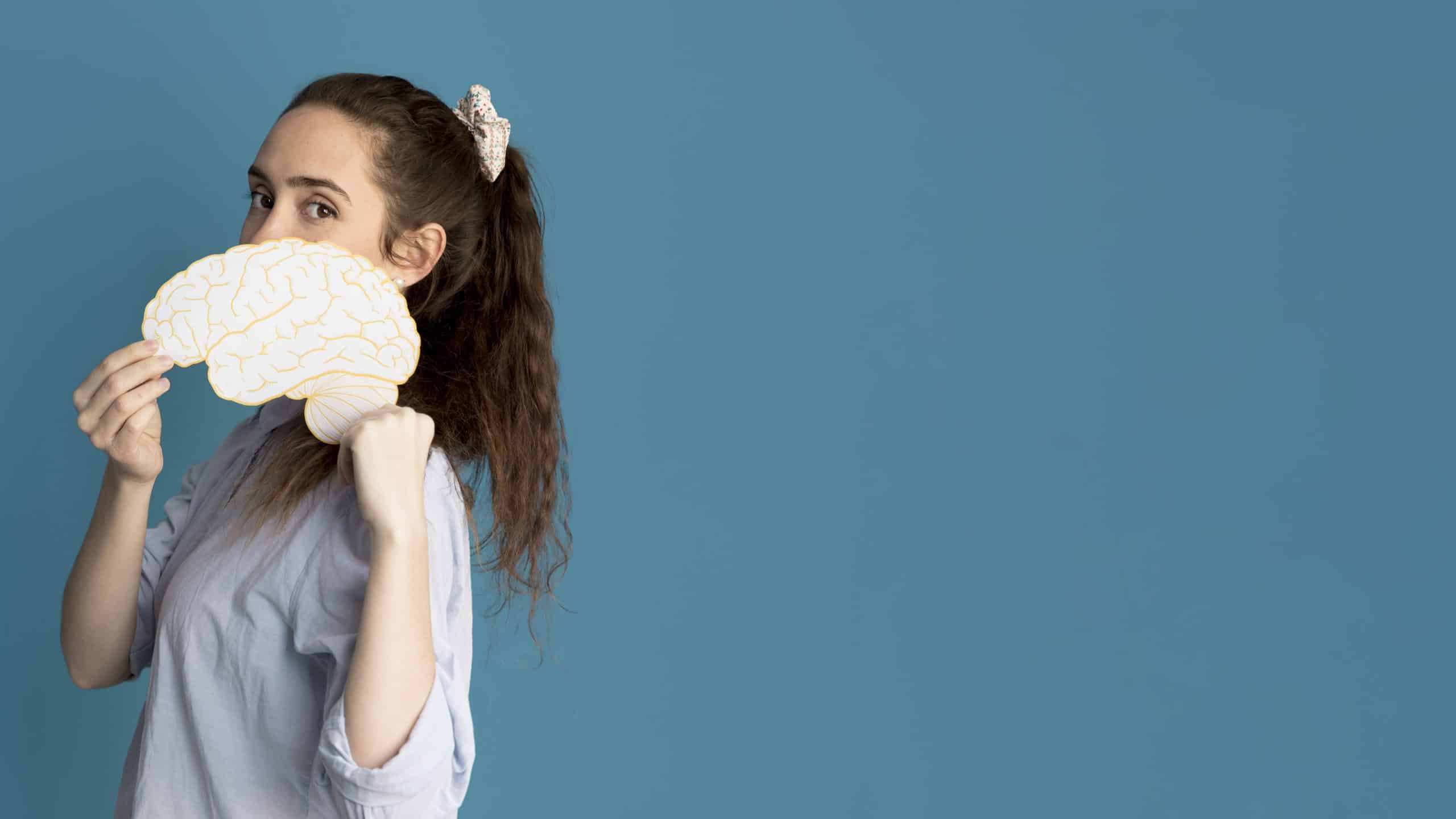 Mulher jovem com cabelo preso segura um cérebro de papel desenhado em fundo azul
