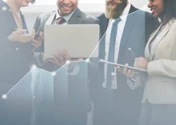 Equipe de profissionais de diferentes áreas analisando dados em notebook com gráfico de crescimento ascendente sobreposto.