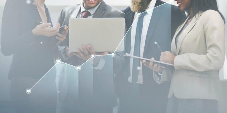 Equipe de profissionais de diferentes áreas analisando dados em notebook com gráfico de crescimento ascendente sobreposto.