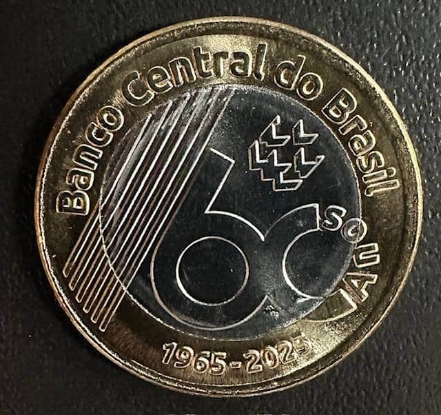 Moeda de 1 Real do Banco Central (BC) de 60 anos (1965-2025). O exemplar comemorativo deve ser verificado quanto ao estado de conservação (Flor de Cunho) e a possíveis defeitos para ter valor real.