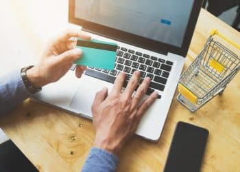 Pessoa segurando cartão de crédito e digitando no notebook para compra pela internet.