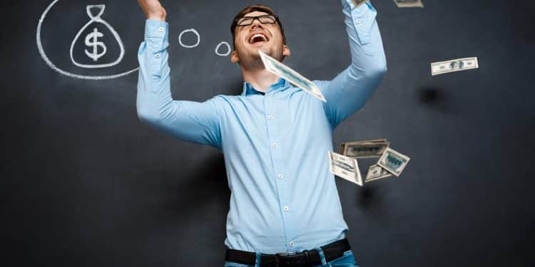 Homem de camisa azul joga notas de dinheiro ao ar com desenho de saco de dinheiro ao fundo Legenda: Homem alegre gesticula enquanto dinheiro voa no ar, simbolizando sucesso financeiro e realização de sonho.