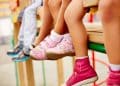 Close nas pernas e pés de crianças com tênis rosa e vermelho sentadas em banco no playground.