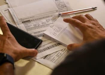 Pessoa organizando boletos bancários e documentos financeiros sobre mesa