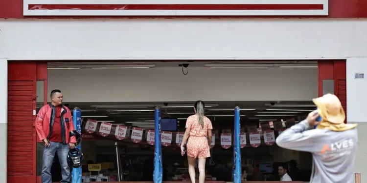 Entrada da Lojas Americanas com pessoas à frente e banners promocionais no interior da loja