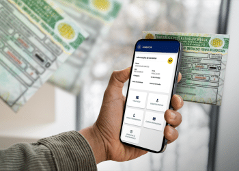 Motorista segurando o celular exibindo informações da CNH digital, com a CNH física visível ao fundo.