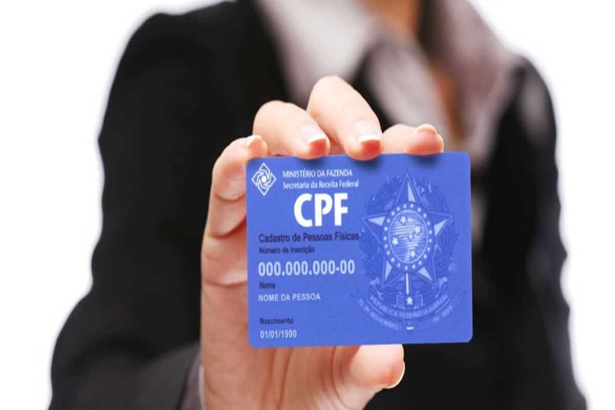 Pessoa segurando cartão azul do CPF da Receita Federal do Brasil com dados fictícios.