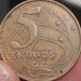 Moeda brasileira de 5 Centavos, ano 2002, em close-up, exemplar conhecido por apresentar o raro erro de cunhagem da data duplicada.