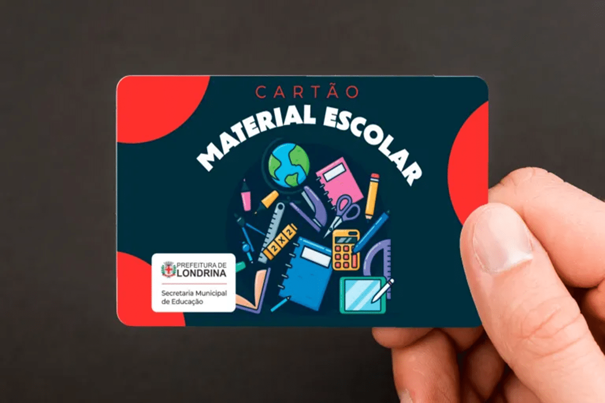 Mão segurando cartão do material escolar da Prefeitura de Londrina com desenhos coloridos de itens escolares.