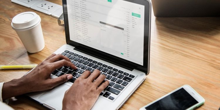 Pessoa escrevendo e-mail profissional em notebook, com foco na candidatura de emprego.