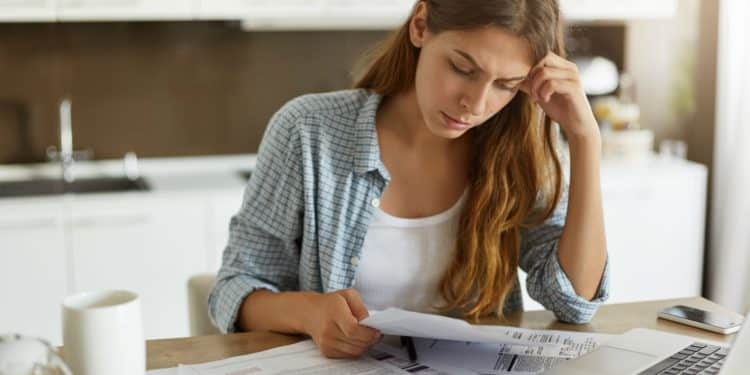 Mulher analisando boletos e contas em casa, preocupada com dívidas e possibilidades de negociação financeira.