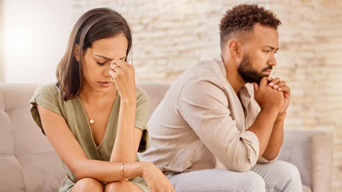 Casal no sofá, com a mulher quieta e expressão de frustração enquanto o homem parece pensativo.