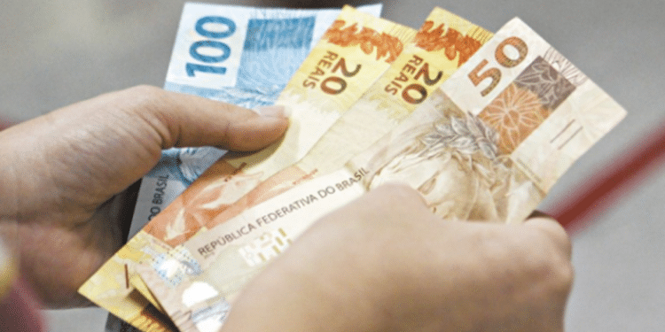 Duas mãos segurando notas de dinheiro em reais, incluindo cédulas de 100, 50 e 20 reais.