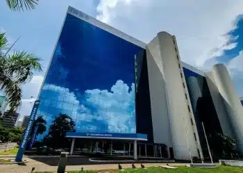 Fachada de um edifício da Previdência Social (INSS) com vidros espelhados refletindo o céu, representando o pagamento de benefícios.