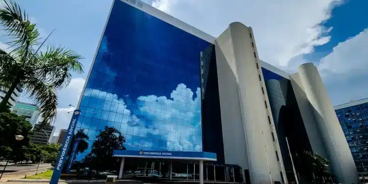 Fachada de um edifício da Previdência Social (INSS) com vidros espelhados refletindo o céu, representando o pagamento de benefícios.