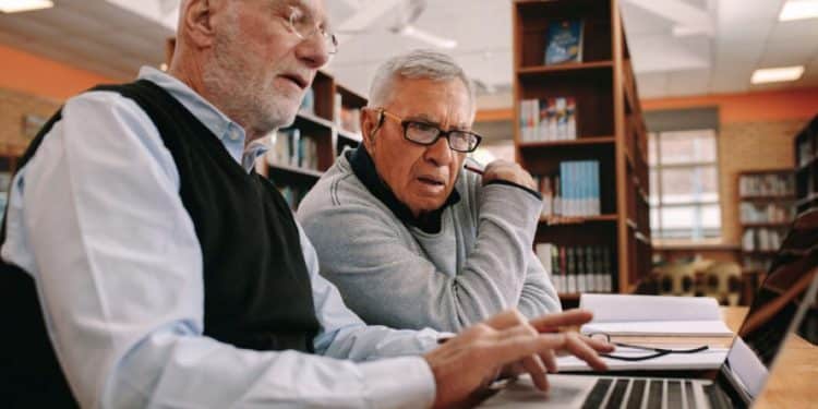 Dois homens maduros trabalhando juntos em frente ao computador em ambiente de estudo, em busca de novas profissões.