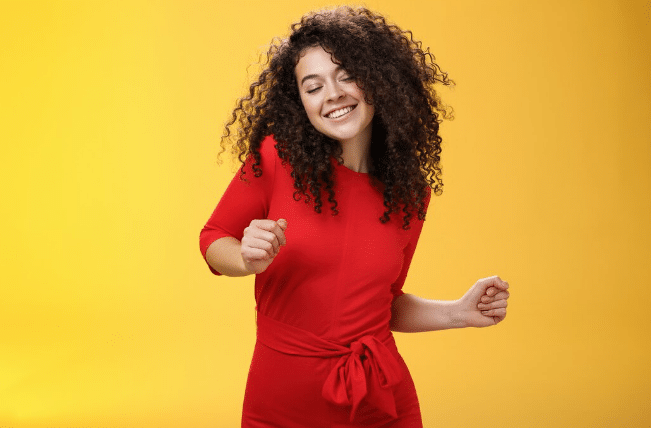 Mulher jovem sorridente com cabelo cacheado usando vestido vermelho contra fundo amarelo