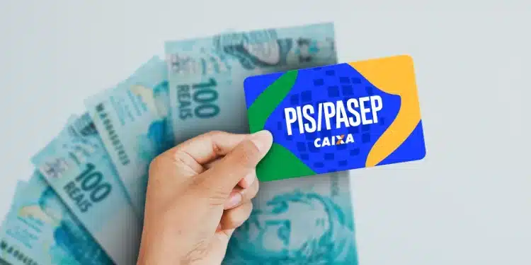 Mão segurando cartão PIS/PASEP da Caixa em frente a notas de 100 reais
