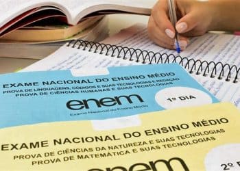 Cadernos de prova do Enem com material de estudo e mão escrevendo.