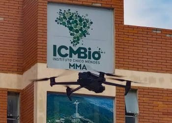 Drone preto voando próximo à fachada de tijolos do prédio do ICMBio com seu logotipo visível