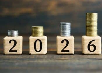 Quatro blocos de madeira formando o ano 2026 com pilhas de moedas crescentes sobre cada um.