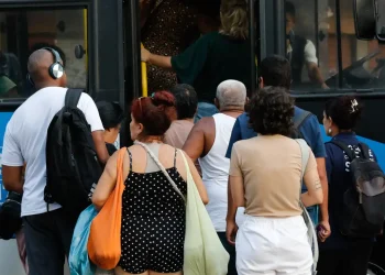 Pessoas de diferentes idades esperando e entrando em ônibus público em ambiente urbano